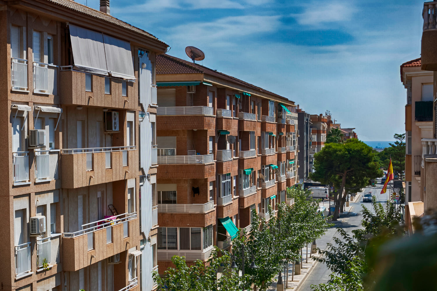 Bloque de viviendas con balcones junto a una calle arbolada